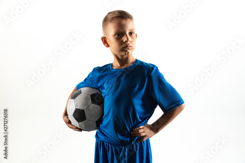 Young boy as a soccer or football player in sportwear standing with the ball like a winner, the best forward or goalkeeper on white background. Fit playing boy in action, movement, motion at game.
