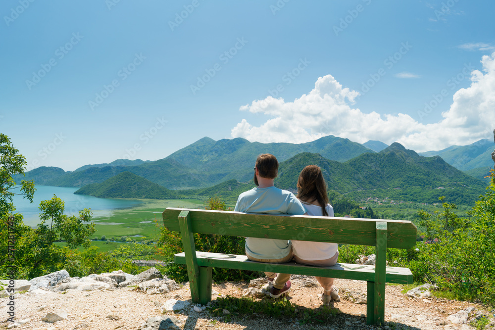 couple sits on a bench and admires the view of the lake and hills couple sits on a bench and admires the view of the lake and hills