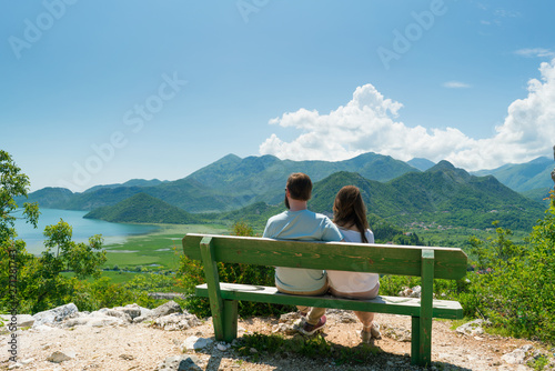 couple sits on a bench and admires the view of the lake and hills