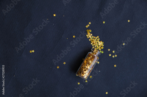 Bottle with gold stars spangles and for decoration, festive decoration on a dark background