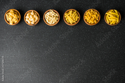 Fototapeta Naklejka Na Ścianę i Meble -  Assortment of different dry pasta types against black background, top view with copy space. Concept of Italian food and food background.