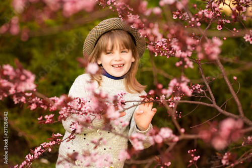 Spring portrait, adorable little girl in hat walk in blossom tree garden on sunset