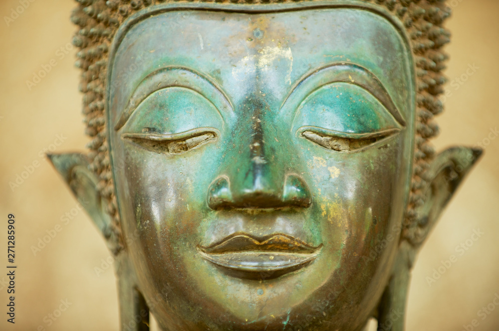 Close up of a face of an ancient copper Buddha statue outside of the Hor Phra Keo temple (former temple of the Emerald Buddha) in Vientiane, Laos.