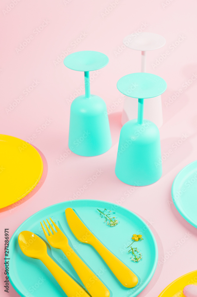 Bright colored plastic picnic utensils. Pink, yellow, blue colors in the bowl. Photo in hard light. Copy space