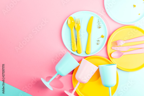 Bright colored plastic picnic utensils. Pink, yellow, blue colors in the bowl. Photo in hard light. Copy space