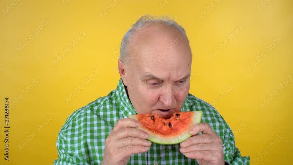 Portrait of happy elderly man standing isolated on orange background and eating juicy watermelon while looking at camera Portrait of happy elderly man standing isolated on orange background and eating juicy watermelon while looking at camera