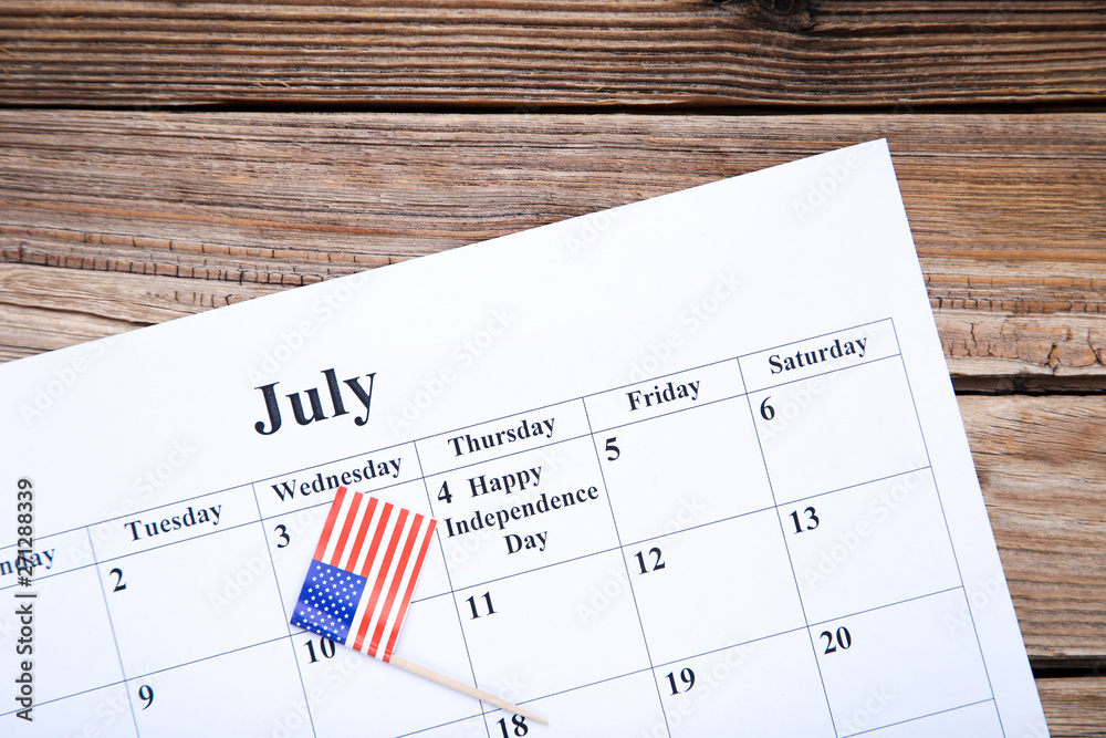 Text Happy Independence Day in calendar with american flag on brown wooden table Text Happy Independence Day in calendar with american flag on brown wooden table