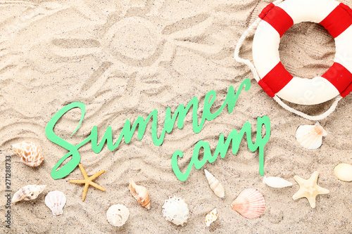 Paper text Summer camp with seashells and lifebuoy on beach sand