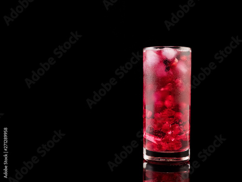 Sweet pomegranate with ice and berry on black background. Delicious summer red lemonade/cold tea.