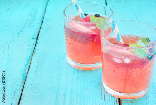 Delicious summer  lemonades with ice,berry, peach and lime on wooden background. Two glass with cold, fresh drink or coctail on blue table