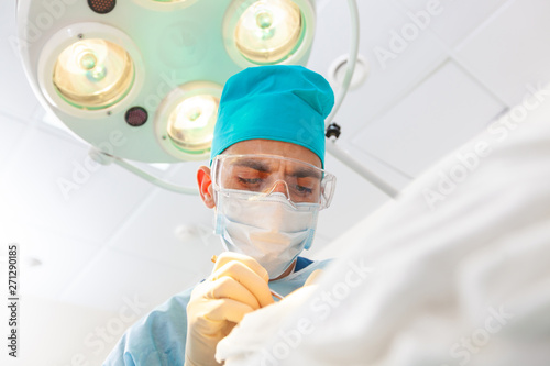 Beautiful portrait of a surgeon doctor at work. The lamp in the background. The surgeon gives injections to the head. Baldness treatment. Hair transplant. Surgeons in the operating room carry out hair