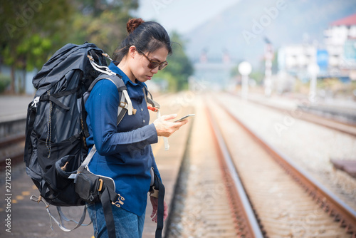 Backpacker asian woman in casual dress and bag on,wait for the railway train hand hold smart mobile phone with copy space.