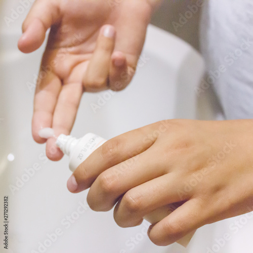 Hands of a young girl squeeze white cream on a finger over the sink