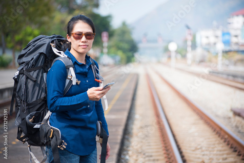 Backpacker asian woman in casual dress and bag on,wait for the railway train hand hold smart mobile phone with copy space.