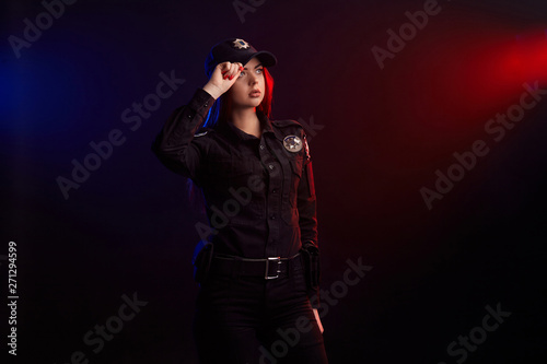 Photography Serious female police officer is posing for the camera against a black background with red and blue backlighting