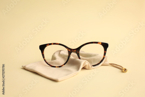 Modern fashionable acetate spectacles, torture color with textile beige bag laying on light yellow background. photo