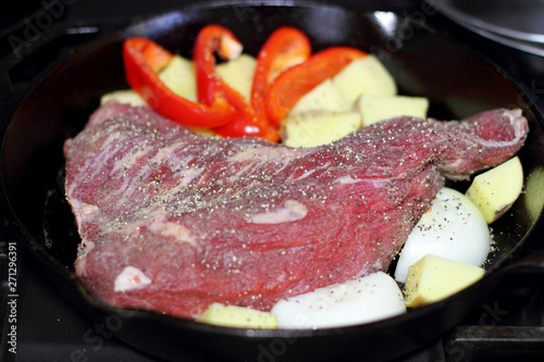 Sirloin tritip steak in a cast iron pan with potatoes and onions on the stove top.