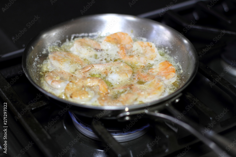 Shrimp scampi cooking in butter and garlic in a stainless steel skillet on the stove. Shrimp scampi cooking in butter and garlic in a stainless steel skillet on the stove.