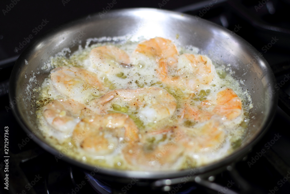 Shrimp scampi cooking in butter and garlic in a stainless steel skillet on the stove. Shrimp scampi cooking in butter and garlic in a stainless steel skillet on the stove.
