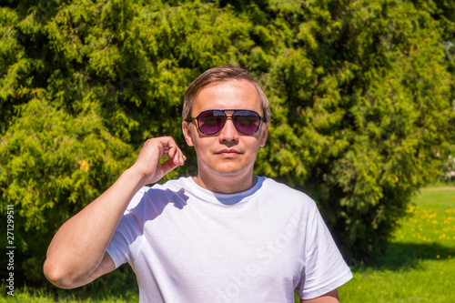 Portrait of a man in sunglasses and a white T-shirt standing outside in park