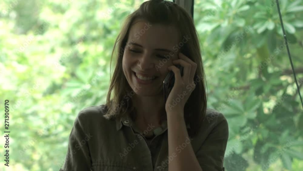 Young happy woman talking on cellphone by the window in kitchen Young happy woman talking on cellphone by the window in kitchen