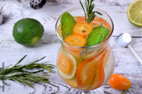 Sparkling beverage with slices of lime, kumquat and orange topped with mint against the white wooden background