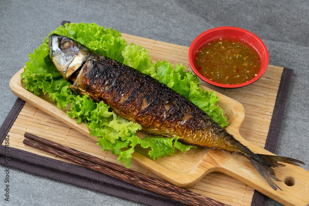 Grilled Saba Fish in wooden dish with seafood sauce on table. Grilled Saba Fish in wooden dish with seafood sauce on table.
