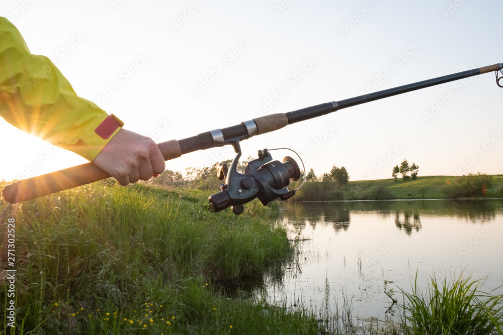 Fishing rod on the lake bent under the weight of fish at sunset. Fishing  Rod Sunset Rays Stock Photo