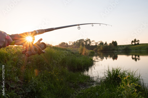 Fishing rod on the lake bent under the weight of fish at sunset. Fishing Rod Sunset Rays