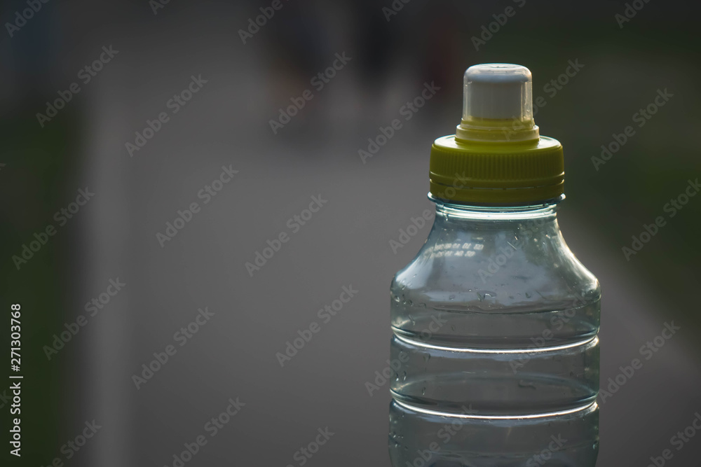 Plastic bottle top full with water with yellow cap in a park or garden with green trees in blurred background Recyclable beverage container that protects the nature