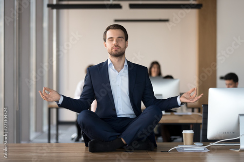 Peaceful businessman meditating with eyes closed at workplace