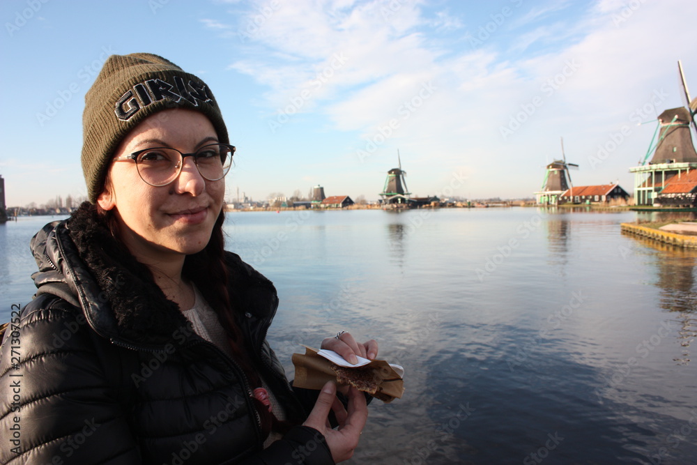 Caucasian tourist girl dressed in winter clothes walks among the canals of the Zaan river, in Zaansche Schans, among the old Dutch windmills Caucasian tourist girl dressed in winter clothes walks among the canals of the Zaan river, in Zaansche Schans, among the old Dutch windmills