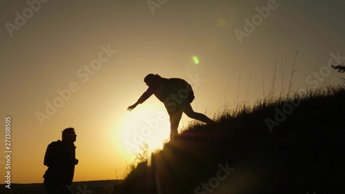 Fototapeta Naklejka Na Ścianę i Meble -  woman traveler stretches hand to man climbing to the top of a hill. travelers climb the cliff holding hands. teamwork of business people. Happy family on vacation. tourists hug on top of mountain