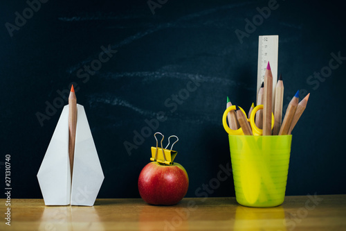Paper plane, fresh apple and colored pencils on chalkboard background.