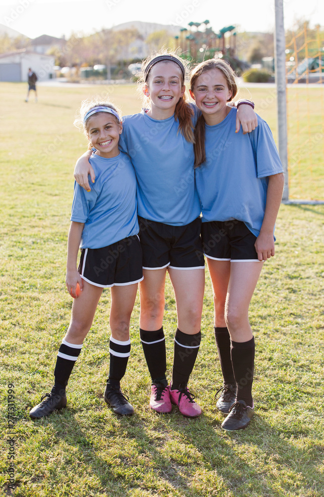 Fototapeta premium Portrait of smiling confident girls standing on soccer field