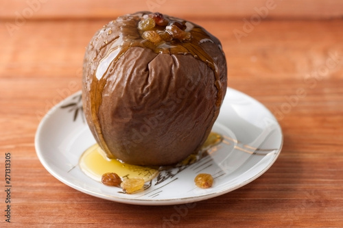 Baked apple stuffed with raisins and walnuts and honey poured on a white plate on a wooden background.