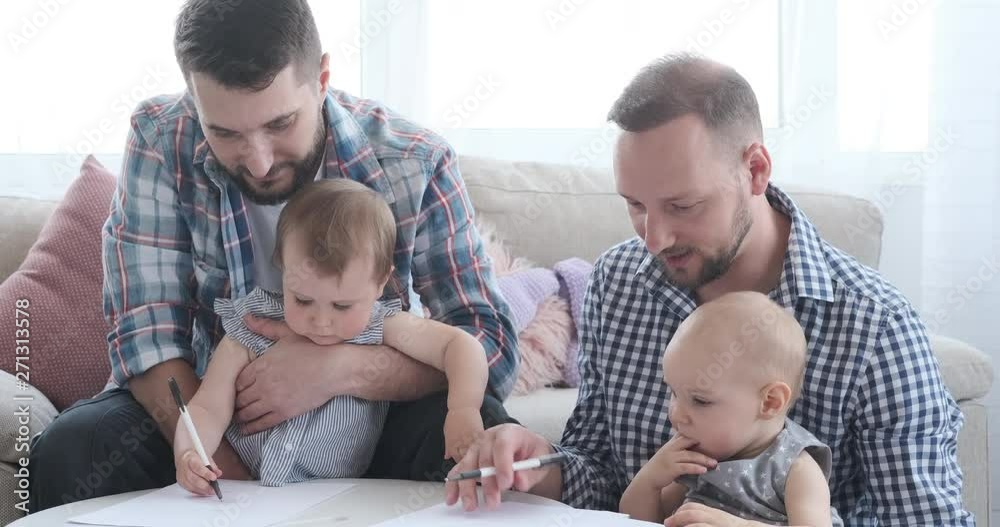 Two young fathers helping baby daughters to draw on paper Two young fathers helping baby daughters to draw on paper