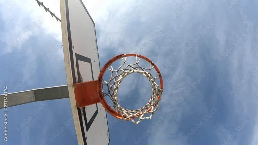 SLOWMO rotating view bellow the basketball hoop looking at the sky with