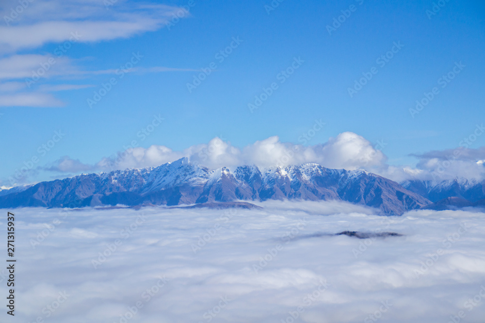 Fototapeta premium Low clouds or fog (inversion) above lake Wakatipu and Queenstown valley. View of the scenic road and snow covered peaks of Single cone, Cecil Peak and Mount Nicholas. Panoramic landscape. New Zealand.