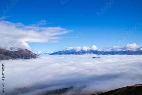 Low clouds or fog  inversion  above lake Wakatipu and Queenstown valley. View of the scenic road and snow covered peaks of Single cone  Cecil Peak and Mount Nicholas. Panoramic landscape. New Zealand.