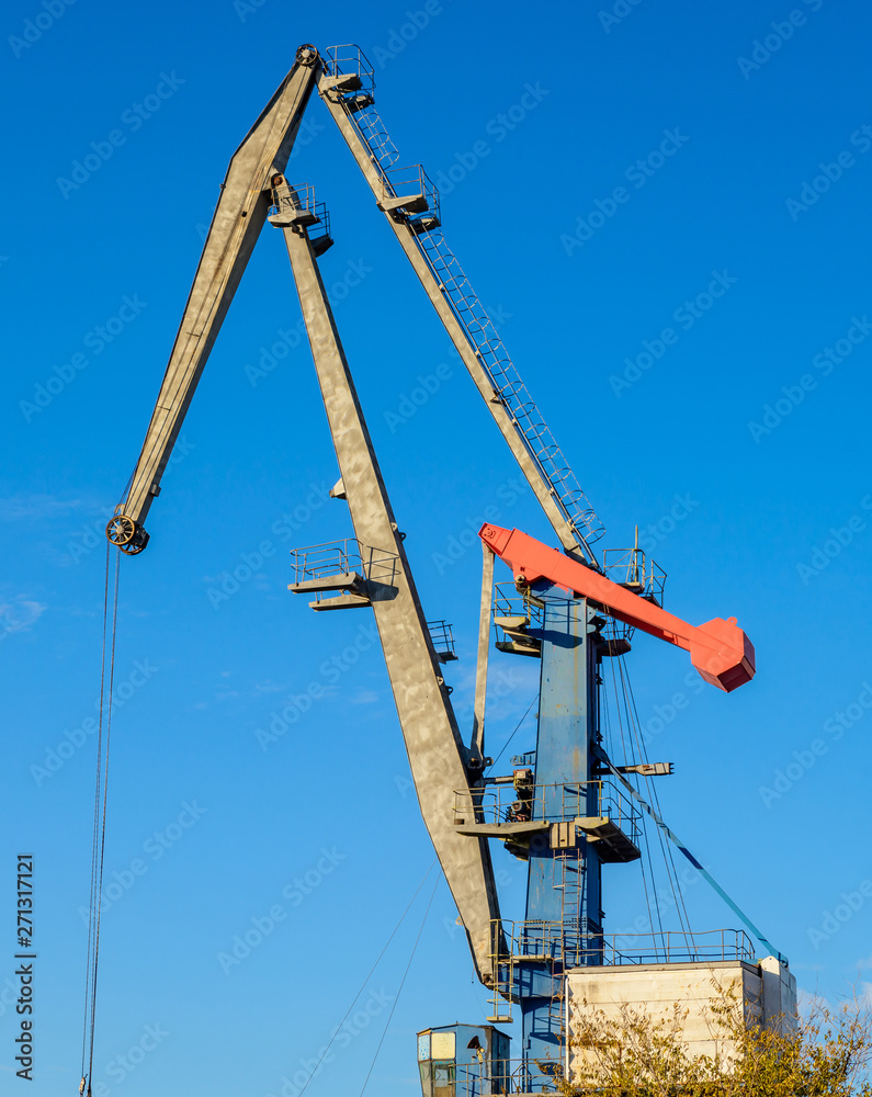 Large iron port crane while working on blue sky background. Large iron port crane while working on blue sky background.