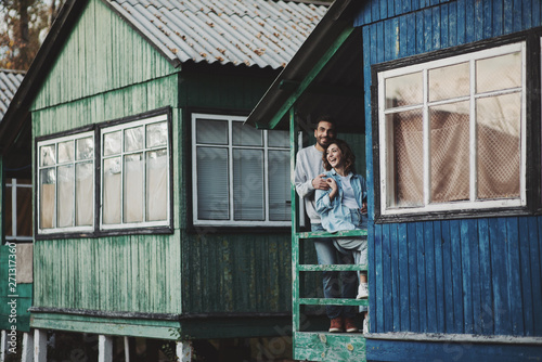 Smiling couple standing on porch of wooden cabin. © Olena Bloshchynska