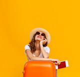concept of travel. happy woman girl with suitcase and passport on yellow background.
