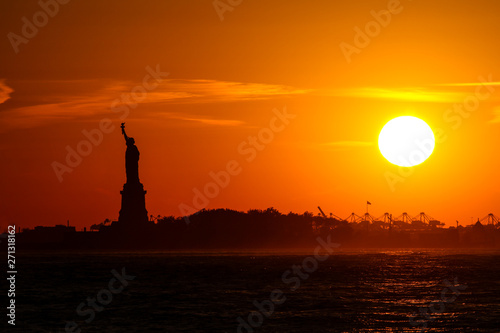 statue of liberty at sunset with silhouette and sun and orange sky