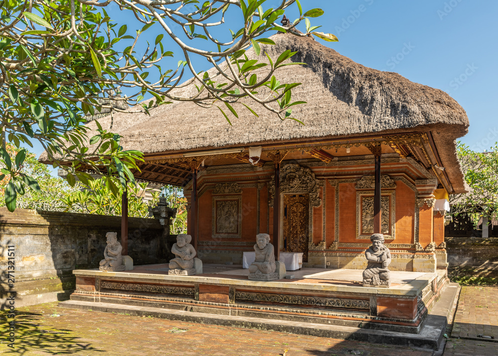 Ubud, Bali, Indonesia - February 26, 2019: Batuan Temple. Large closed shrine with reed roof set on courtyard under blue sky. Gray stone statues and green foliage. Ubud, Bali, Indonesia - February 26, 2019: Batuan Temple. Large closed shrine with reed roof set on courtyard under blue sky. Gray stone statues and green foliage.