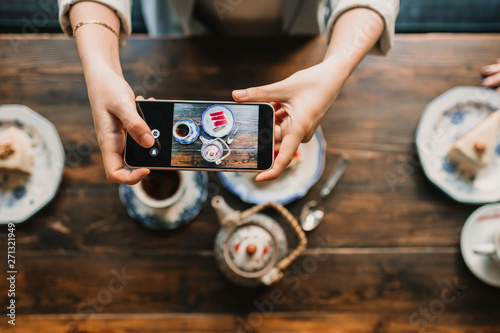 Top view of woman taking a photo of cake and tea in coffee shop