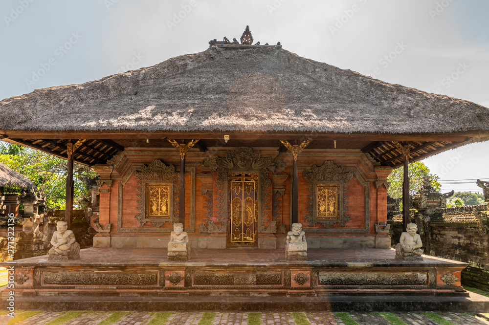 Ubud, Bali, Indonesia - February 26, 2019: Batuan Temple. Large closed shrine with reed roof set on courtyard under blue sky. Gray stone statues and green foliage. Ubud, Bali, Indonesia - February 26, 2019: Batuan Temple. Large closed shrine with reed roof set on courtyard under blue sky. Gray stone statues and green foliage.