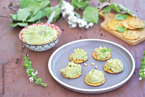 Snack, green pea spread with almonds and basil on unsweetened crackers on a brown clay plate. Healthy snacks.