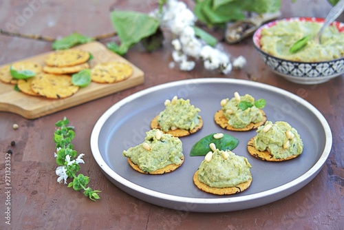 Snack, green pea spread with almonds and basil on unsweetened crackers on a brown clay plate. Healthy snacks.