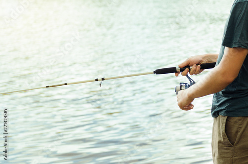 A man in a t-shirt and dark pants is fishing on the lake on a summer day with a white fishing rod with a reel. Concept active leisure.